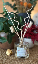 Load image into Gallery viewer, Diffuser in the Spokane Autumn Leaves scent with decorative wood reeds on a table with foliage and flowers in the background