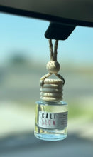 Load image into Gallery viewer, The Cali Glow Car Diffuser from the Coastal Collection is shown hanging from the rearview mirror.