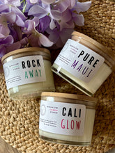 Load image into Gallery viewer, Three candles with labels 'Rock Away', 'Pure Maui', and 'Cali Glow' on a woven surface with flowers.