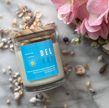 Load image into Gallery viewer, Candle in clear jar with wooden lid in the scent of 'DEL RAY' from Bungalow's Florida Collection sitting on a marble table surrounded by seashells and pink flowers.