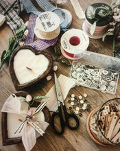 Load image into Gallery viewer, Crafting materials including heart-shaped candles, scissors, ribbons, and buttons on a wooden table, ready for a candle making class.