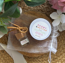 Load image into Gallery viewer, A car diffuser and 4oz mini candle in the Peony & Nectar scent, on top of a white mesh drawstring bag that it will be bundled in.