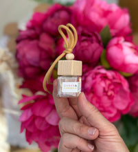 Load image into Gallery viewer, A Bungalow car diffuser in the Guava & Gardenia scent being held in front of pink flowers.