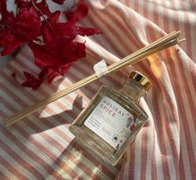 Load image into Gallery viewer, Glass reed diffuser jar in the Holiday Spice scent laying on a red stripped cloth with wood reeds next to it in a bundle.