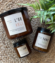 Load image into Gallery viewer, 3 Sizes of candles from the Kitchen Collection in amber-colored jars sitting on a woven mat.
