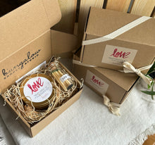 Load image into Gallery viewer, A gift set containing a LOVE soy candle and safety matches in an apothecary jar, sitting in a brown Kraft box and other boxes wrapped in ribbon stacked next to it.