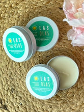 Load image into Gallery viewer, Three travel candle tins with a green label in the Las Olas scent on a woven surface with flowers.