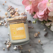 Load image into Gallery viewer, Candle in clear jar with wooden lid in the scent of 'Lauderdale' from Bungalow's Florida Collection sitting on a marble table surrounded by seashells and pink flowers.