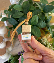 Load image into Gallery viewer, A Bungalow car diffuser in the Lemon & Basil scent being held in front of a plant.