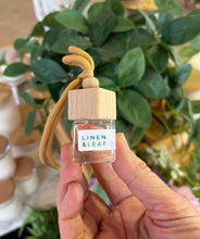 Load image into Gallery viewer, A Bungalow car diffuser in the Linen & Leaf scent being held in front of a plant.