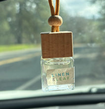 Load image into Gallery viewer, A Bungalow car diffuser in the Linen & Leaf scent hanging from the car rearview mirror.
