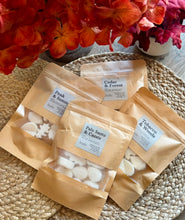 Load image into Gallery viewer, 4 packages of wax melts in Kraft paper bags with labels for the Cascade Collection scents on a woven surface with flowers in the background