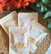 Load image into Gallery viewer, 4 Packages of Wax Melts in white packaging with a window sitting on a mat in front of orange fall flowers.