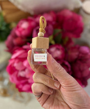 Load image into Gallery viewer, A Bungalow car diffuser in the Peony & Nectar scent being held in front of pink flowers.