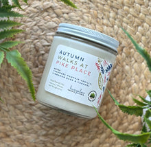 Load image into Gallery viewer, Glass candle jar labeled with scent 'Autumn Walks at Pike Place' on a woven surface with plants around.
