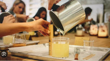 Load image into Gallery viewer, A candle-making class participant pouring hot wax into candle jar.