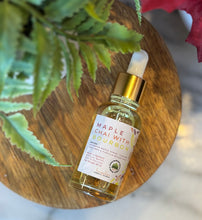 Load image into Gallery viewer, Bottle with dropper lid of 'Maple Chai with Bourbon' scented fragrance oil on a wooden surface with flowers in the background