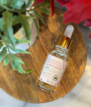 Load image into Gallery viewer, Bottle with dropper lid of 'Spokane Sweater Weather' scented fragrance oil on a wooden surface with flowers in the background