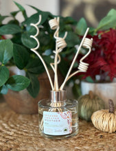 Load image into Gallery viewer, Diffuser in the Spokane Sweater Weather scent with decorative wood reeds on a table with plants and pumpkins in the background