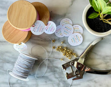 Load image into Gallery viewer, The unique round tags of the 4 oz embossed jar candles are shown with string and metal hooks.