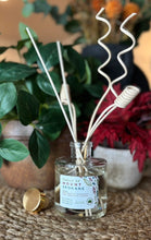 Load image into Gallery viewer, Diffuser in the Trails of Mount Spokane scent with decorative wood reeds on a table with foliage and flowers in the background
