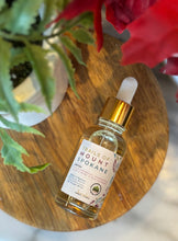 Load image into Gallery viewer, Bottle with dropper lid of 'Trails of Mount Spokane' scented fragrance oil on a wooden surface with flowers in the background.