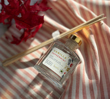Load image into Gallery viewer, Glass reed diffuser jar in the Vanilla Peppermint scent laying on a red stripped cloth with wood reeds next to it in a bundle.