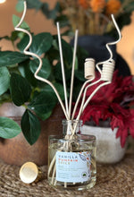 Load image into Gallery viewer, Diffuser in the Vanilla Pumpkin Spice scent with decorative wood reeds on a table with foliage and flowers in the background