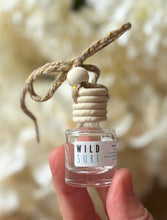 Load image into Gallery viewer, Car diffuser in a small apothecary bottle in the Wild Surf scent, held in a hand in front of a green leafy background.