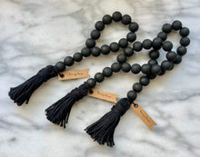 Load image into Gallery viewer, Three matte black wood bead garlands for wine bottles on a marble surface.