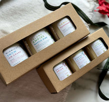 Load image into Gallery viewer, Two cardboard gift boxes with open windows, displaying multiple 3 candles inside. The boxes are presented on a white fabric surface with a green ribbon to the side.