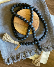 Load image into Gallery viewer, A string of Mango Wood Contentment Beads hand-painted in matte black and draped on a table as home decor.