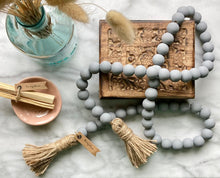 Load image into Gallery viewer, Mango Wood Contentment Bead string, hand painted in Gray, with jute tassels. Staged with burn sticks and draped on a jewelry box.