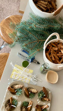 Load image into Gallery viewer, Counter filled with organic fire starter makign supplies including pine sprigs, pine cones, cinnamon sticks, wicks, and cupcake holder.