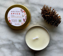 Load image into Gallery viewer, A gold travel tin candle labeled in the scent of Holiday Spice presented open with a pine cone added for decoration.