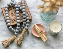 Load image into Gallery viewer, A Mango Wood Contentment Bead string, hand-painted in Gray, with jute tassels, draped on a jewelry box.