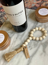 Load image into Gallery viewer, Mango Wood Bead Garland lying on a marble surface next to a wine bottle with gold tin candles also displayed.