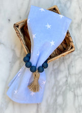 Load image into Gallery viewer, Navy colored mango wood bead napkin holder, holding blue napkin with white stars propped on a basket on a marble table