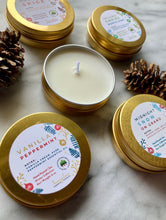 Load image into Gallery viewer, A set of travel tin candles with holiday and winter scents, including vanilla peppermint and rustic pine. The candles are presented in gold metal tins with decorative labels, and some are surrounded by pine cones.