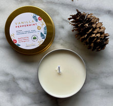 Load image into Gallery viewer, A gold travel tin candle labeled in the scent of Vanilla Peppermint presented open with a pine cone added for decoration.