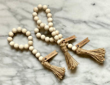 Load image into Gallery viewer, Three natural wood bead garlands for wine bottles on a marble surface.