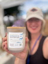 Load image into Gallery viewer, A person in a beige cap holds up a jar candle labeled 'Mountain Mornings in Whitefish' toward the camera, with a blurred outdoor background.
