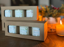 Load image into Gallery viewer, Two cardboard gift boxes with open windows, displaying multiple 3 candles inside. The boxes are presented on a white fabric surface with a green ribbon to the side.
