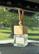 Load image into Gallery viewer, A car diffuser in the Spokane Autumn Leaves scent from the Fall Candle Scent Collection hangs from the car rearview mirror.
