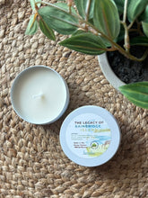 Load image into Gallery viewer, Mini travel candle in a tin with lid on a woven surface, plant in the background, in the scent of The Legacy of Bainbridge Island

