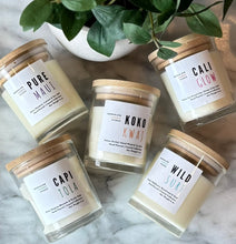 Load image into Gallery viewer, Five candles from the Beachy Coastal Collection in clear glass with wooden lids on a marble surface with a plant in the background.
