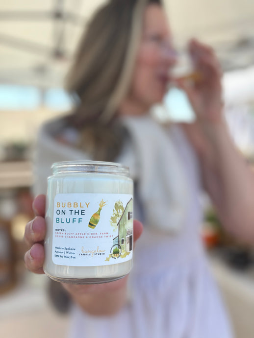 Candle labeled 'Bubbly on the Bluff' held by Bungalow owner, Sue, blurred and sipping bubbly