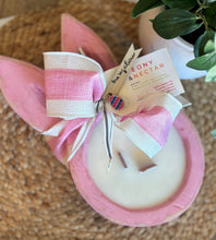 Load image into Gallery viewer, Pinkwash-stained dough bowl candle in the shape of a bunny with pink and white striped ribbon and 'Peony &amp; Nectar' tag on a woven surface
