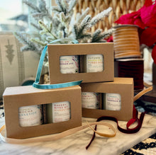 Load image into Gallery viewer, Three sets of two candles in brown window boxes with labels indicating different Fall scents, stacked on a table with a decorative bow and a woven basket in the background.
