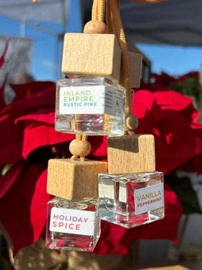 Group of holiday scented car diffusers in front of a poinsettia plant.